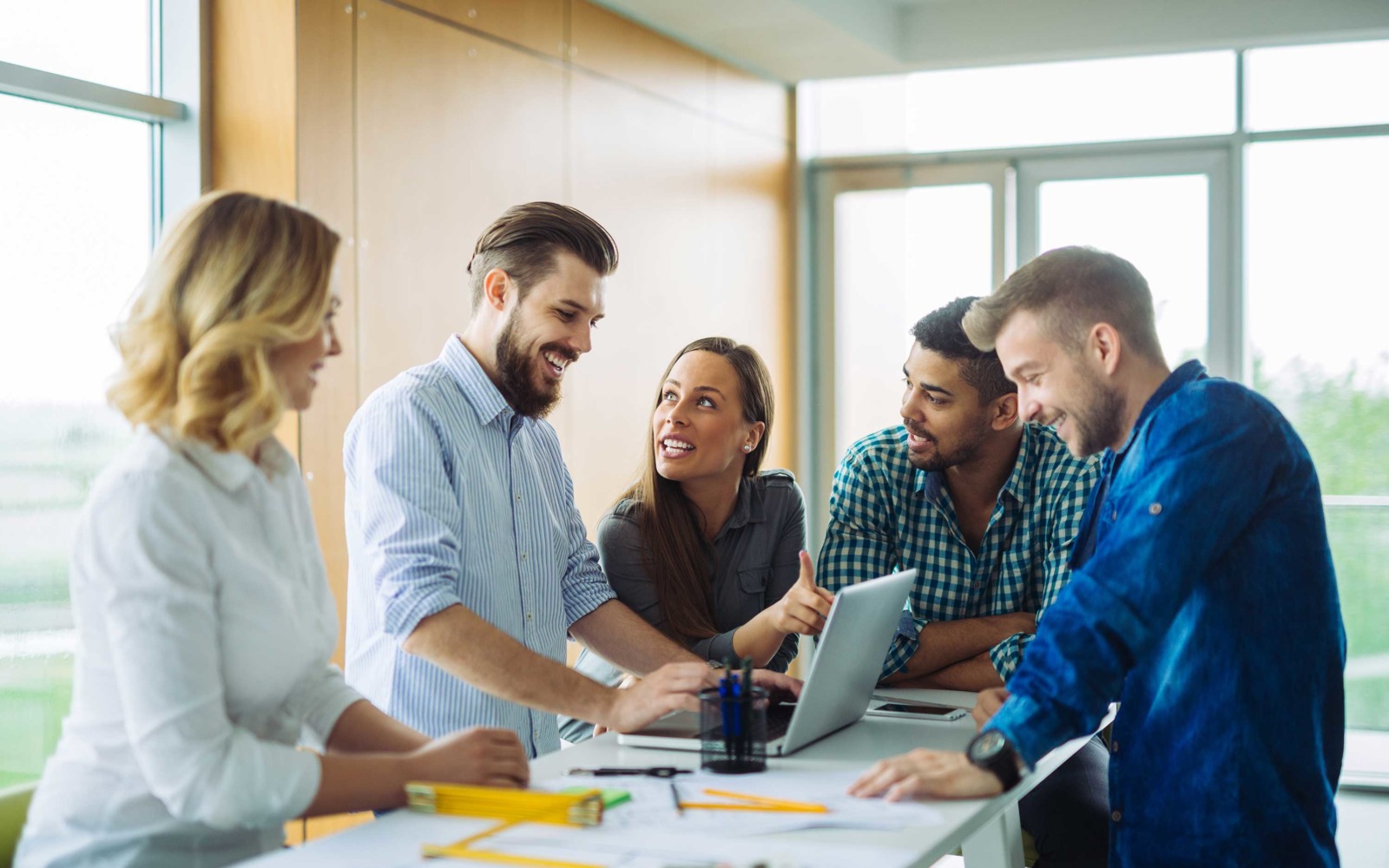 Group of happy young people stood around a laptop discussing work